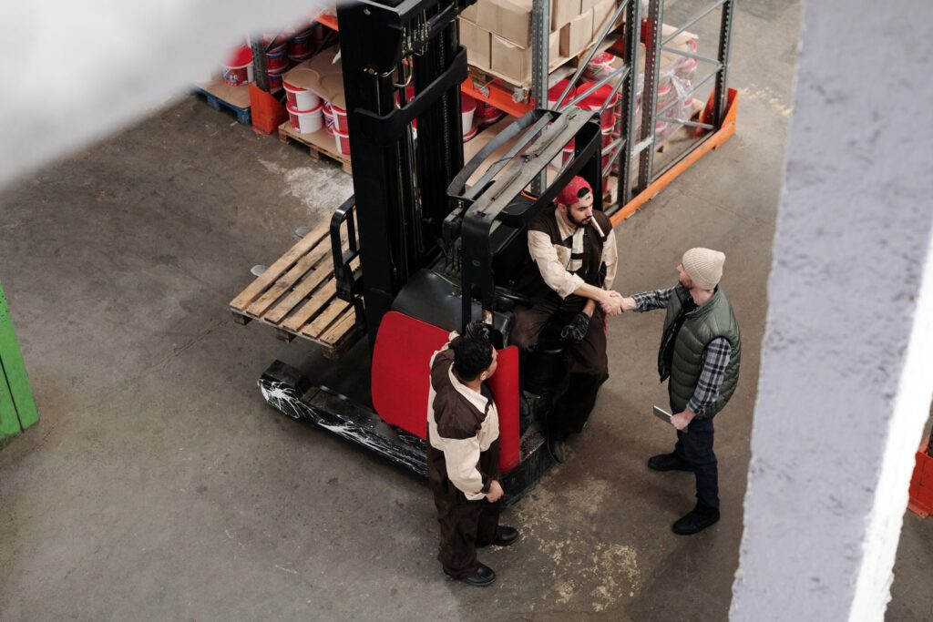 Warehouse workers shaking hands next to a forklift in an industrial setting